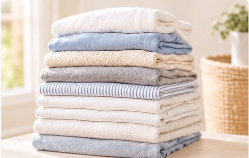 A generous stack of folded laundry in warm cream, soft blue, and grey tones